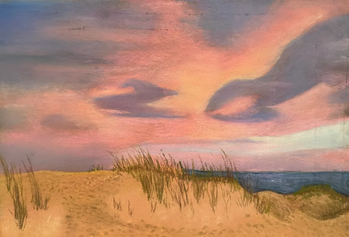 Pink and peach clouds over the ocean, sand dunes, and sparse beach grass