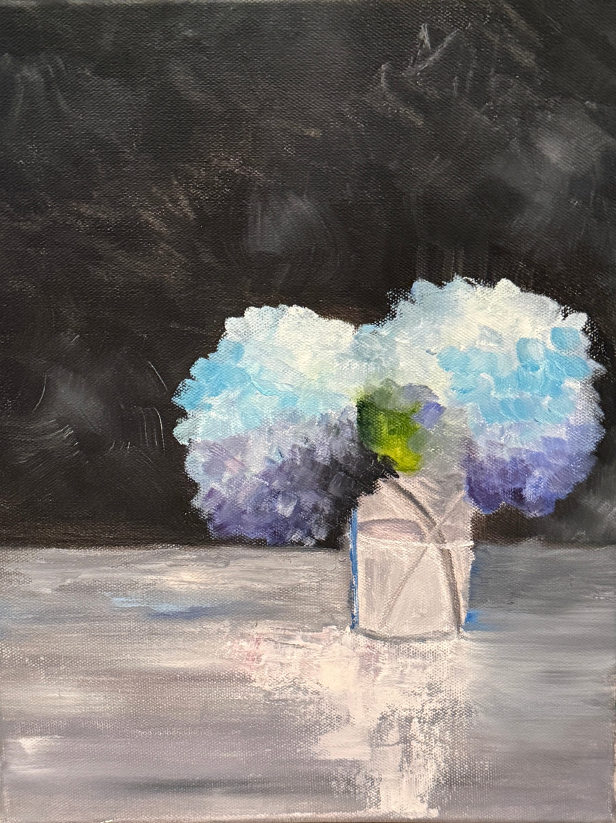 Blue and lavender hydrangea blooms arranged in a white vase against a charcoal background