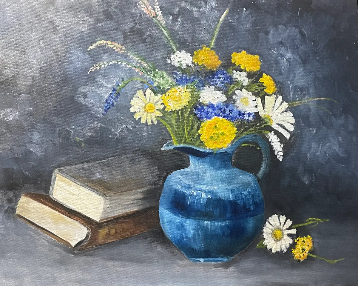 Blue ceramic vase of yellow, white, and blue wildflowers beside two stacked books