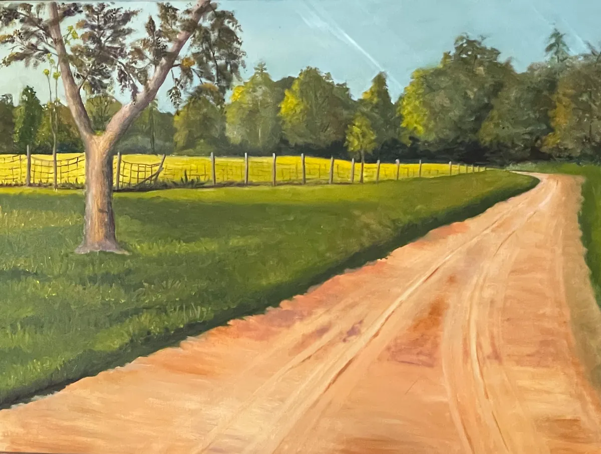 Sandy country road curving past a large tree and fenced green pasture