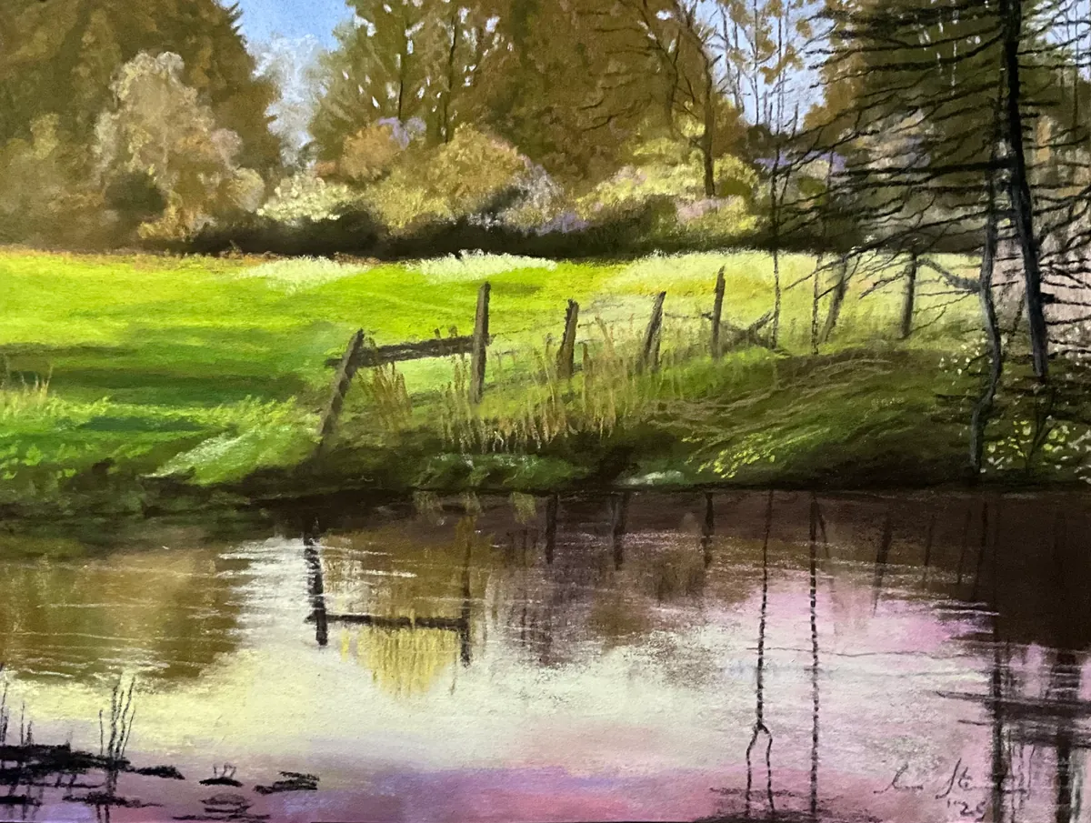 Still pond reflecting fence posts, evergreens, and a bright green pasture