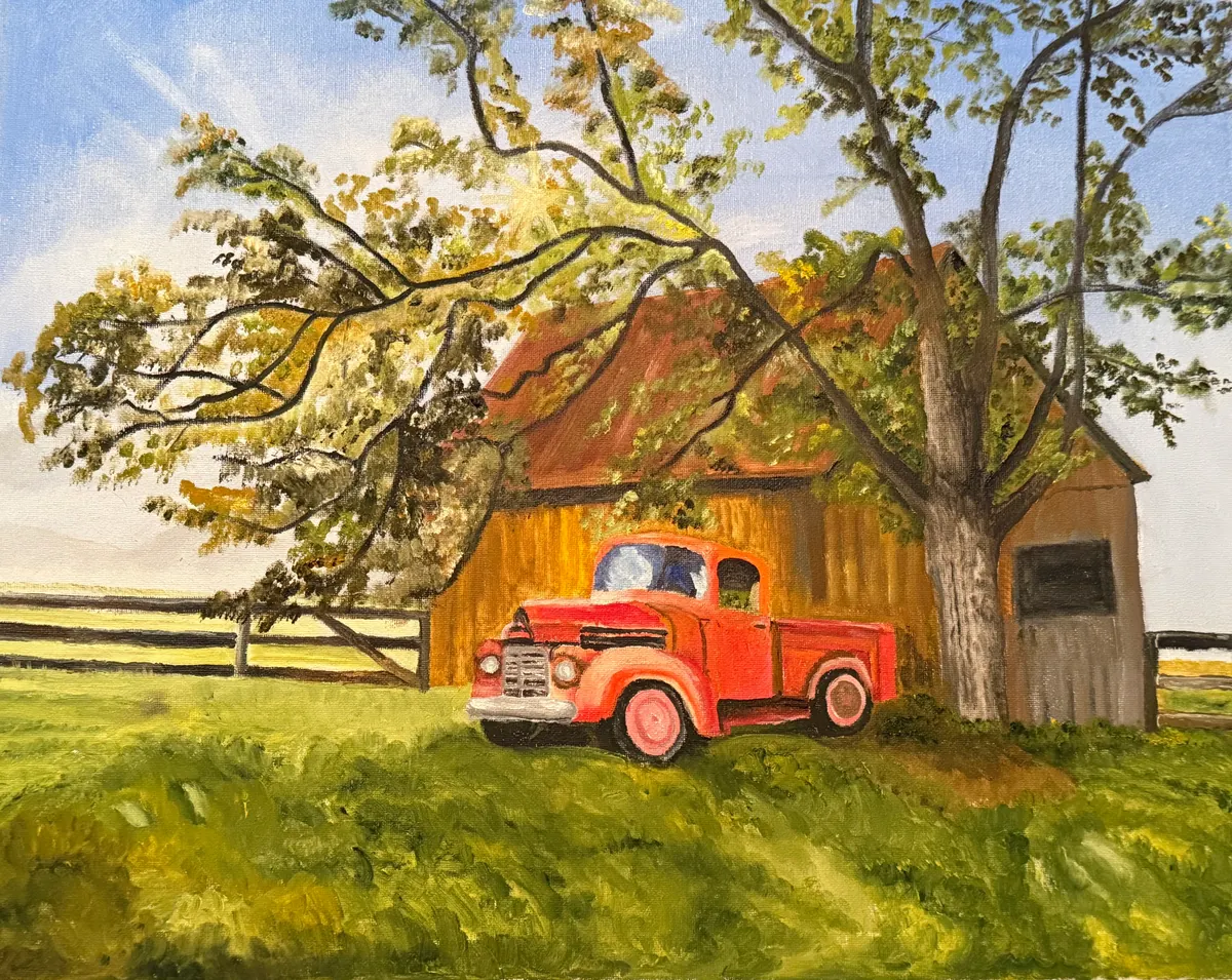 Vintage red pickup parked by a weathered barn beneath a leafy tree