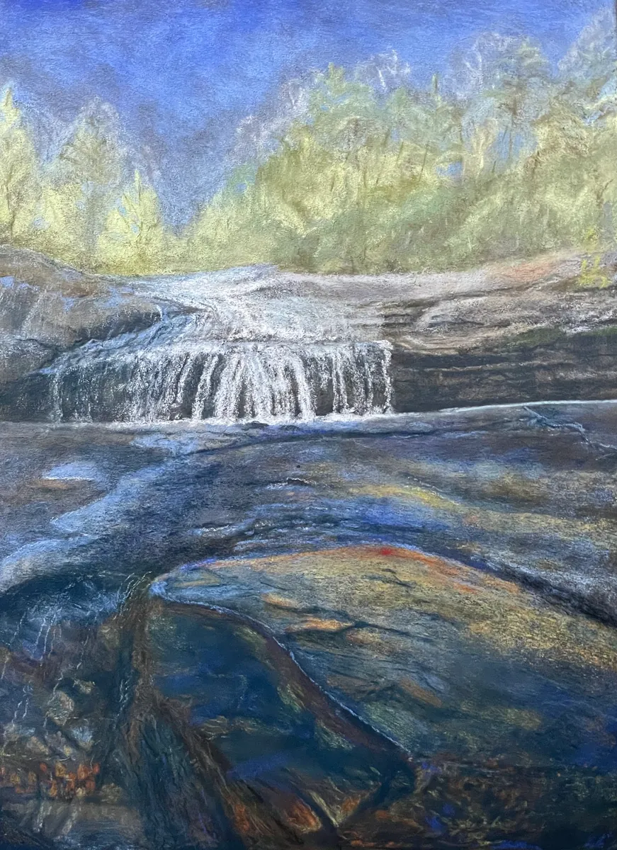 Broad waterfall over dark rock with blue water, large boulders, and pale trees