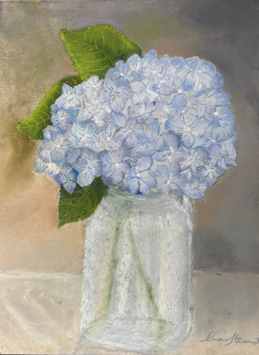 Blue hydrangea blossoms arranged in a clear glass vase against a soft gray background