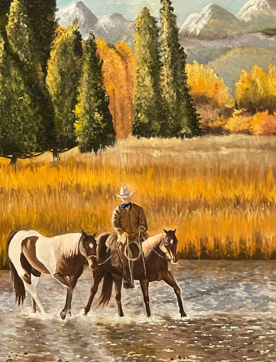 Cowboy guiding two horses across a shallow river amid golden autumn trees and distant snowcapped mountains