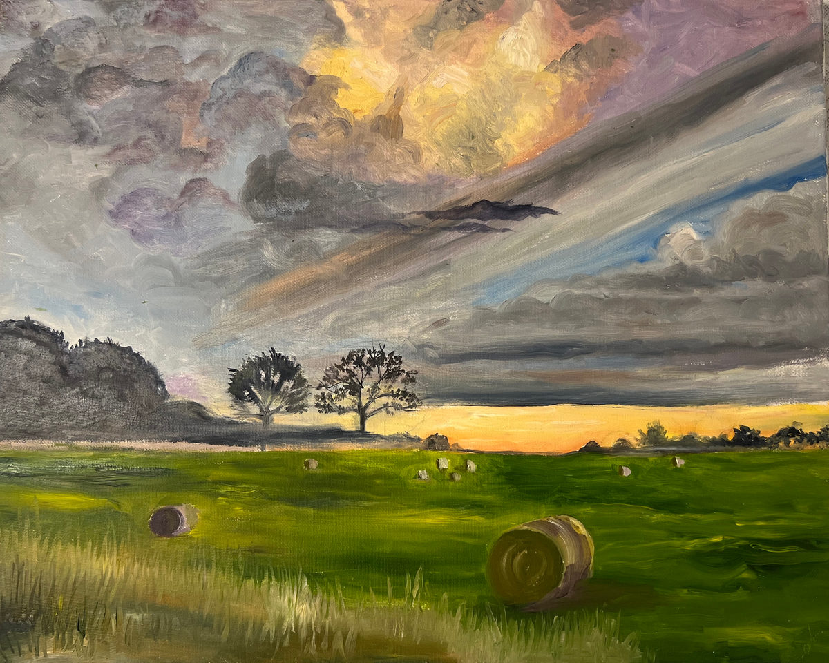 Round hay bales in a green field beneath dramatic gray, violet, and gold sunset clouds