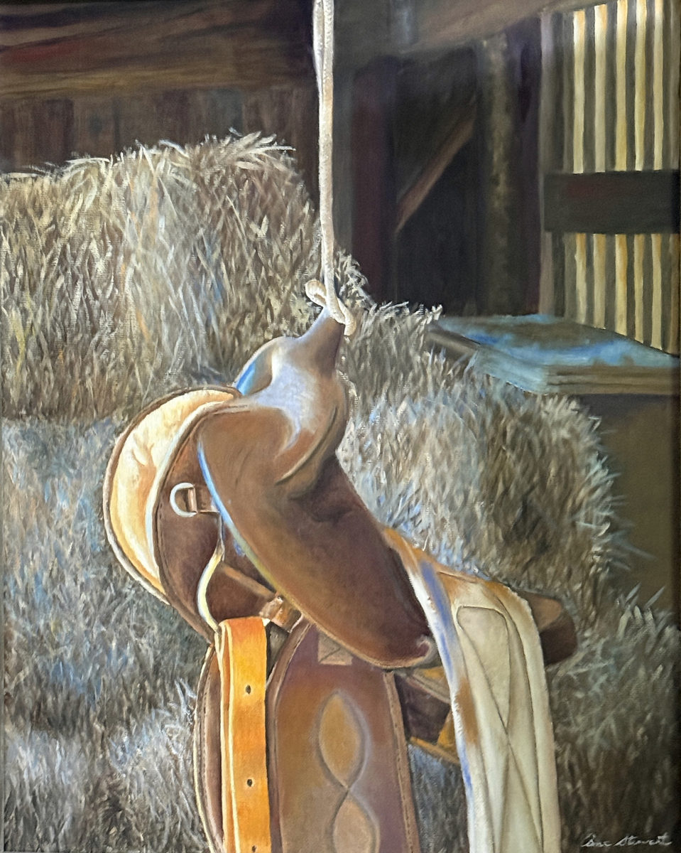 Brown Western saddle resting on hay bales inside a dim wooden barn